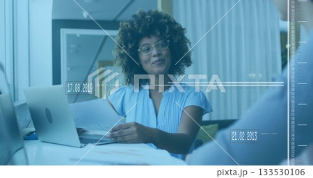 Handling printed documents woman wearing blouse and glasses at meeting table with laptop papers pen Handling printed documents woman wearing blouse and glasses at meeting table with laptop papers pen 133530106