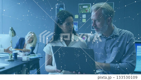 Reviewing professionals in office attire examining laptop screen at corporate office, with monitors Reviewing professionals in office attire examining laptop screen at corporate office, with monitors 133530109