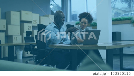 Man in blue shirt and woman in gray sweater collaborating in workspace, with laptop, labeled boxes 133530116