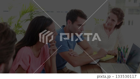 Brainstorming four colleagues using laptop and yellow notepad in meeting room, with colored pencils 133530117