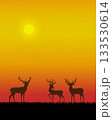 A serene sunset scene with three silhouetted deer standing in a field of grass, against the vibrant orange yellow sky.	 133530614