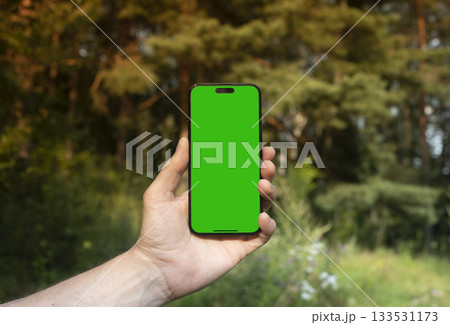 Hand holding mobile phone with empty white screen in front of blurred green forest background. for Hand holding mobile phone with empty white screen in front of blurred green forest background. for 133531173
