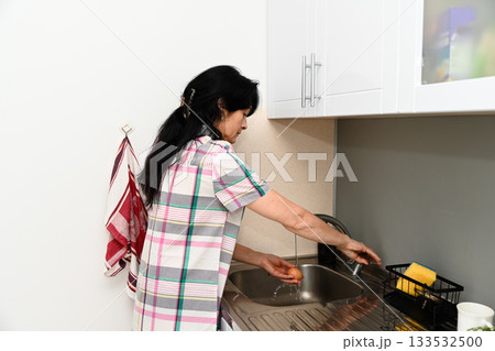 Mature 50 years old Russian woman washing an egg at the sink, focusing on hygiene and food safety, looking calm with visible wrinkles in a home kitchen Mature 50 years old Russian woman washing an egg at the sink, focusing on hygiene and food safety, looking calm with visible wrinkles in a home kitchen 133532500