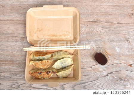crispy fried Gyoza or Japanese dumpling stuffed mashed pork dipping shoyu sauce with wooden chopsticks in brown paper box for take home crispy fried Gyoza or Japanese dumpling stuffed mashed pork dipping shoyu sauce with wooden chopsticks in brown paper box for take home 133536244