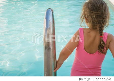 Little girl in swimsuit with a beautiful pool in the background 133536998