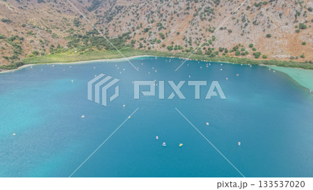 Kournas Lake at foot of mountains crowded with tourists on pedal boats in peak season. 133537020