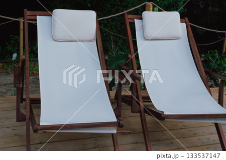 Comfortable lounge chairs with white cushions located in a forest recreation area for enjoying beauty and fresh air Comfortable lounge chairs with white cushions located in a forest recreation area for enjoying beauty and fresh air 133537147