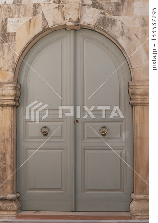 Old grey wooden double door with arched entry and massive ring handles, entrance to a historic building 133537295