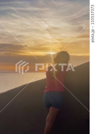 Young girl on terrace observing the magical sunset over Aegean Sea and volcanic caldera of Santorini Young girl on terrace observing the magical sunset over Aegean Sea and volcanic caldera of Santorini 133537373