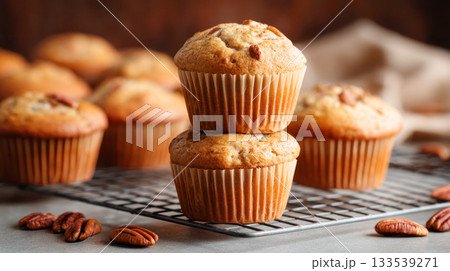 Pecan muffins stacked on a cooling rack, surrounded by scattered nuts, showcasing delicious baked goods in a warm, inviting kitchen atmosphere Pecan muffins stacked on a cooling rack, surrounded by scattered nuts, showcasing delicious baked goods in a warm, inviting kitchen atmosphere 133539271