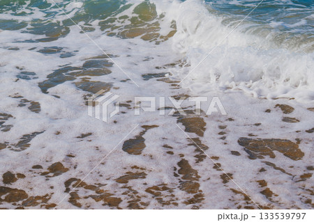 Moment when sea waves roll onto sandy beach creating white foam. Natural marine vacation background Moment when sea waves roll onto sandy beach creating white foam. Natural marine vacation background 133539797