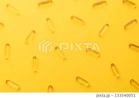 Top view of oil softgel capsules lie in rows diagonal on yellow background. Nutritional supplement contains fish oil, omega 3, omega 6, omega 9, vitamin e, vitamin d and vitamin a. 133540051