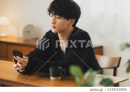 部屋でスマホを見る若い男性 部屋でスマホを見る若い男性 133541004