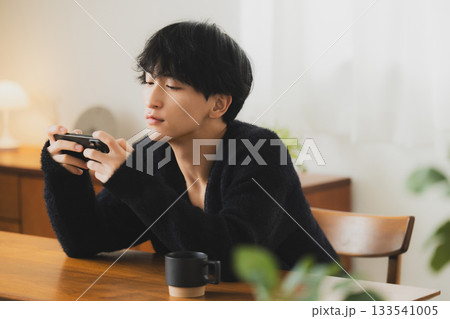 部屋でスマホを見る若い男性　 133541005