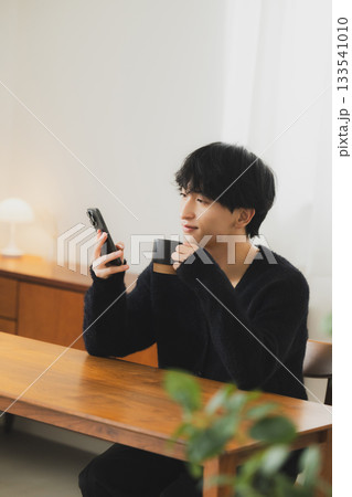 部屋でスマホを見る若い男性　 133541010