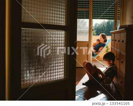 Mother Relaxing on Balcony While Child Plays Indoors Mother Relaxing on Balcony While Child Plays Indoors 133541105