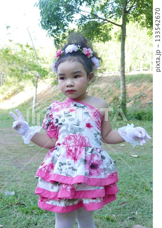 Little Asian girl with beautiful pink dress and flower in her hair in the park 133542670