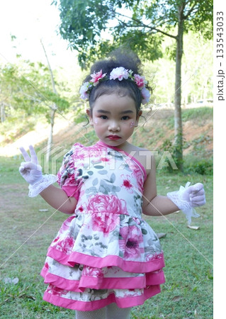 Little Asian girl with beautiful pink dress white gloves and flower in her hair in the park 133543033