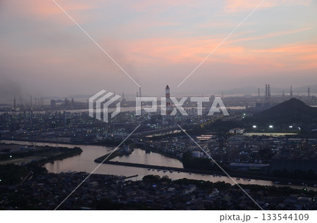 夕暮れに染まる工場夜景と水辺の風景｜産業地帯のシルエットと柔らかな夕焼け空 133544109