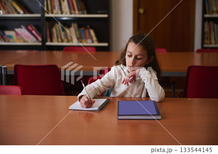 Young Student Writing In Library During Study Time At School Young Student Writing In Library During Study Time At School 133544145