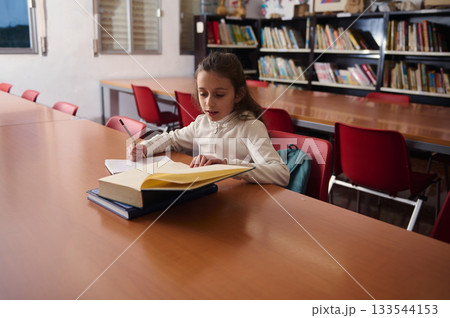 Young Student Studying At Library Table With Books In School, Quiet Learning Moment Young Student Studying At Library Table With Books In School, Quiet Learning Moment 133544153