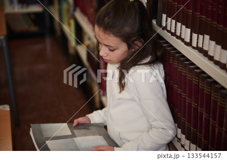 Young Girl Reading a Book in a Library Aisle Exploring Knowledge and Learning 133544157