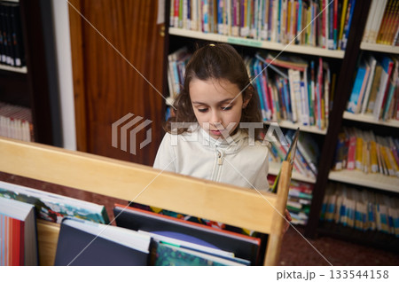 Young Girl Reading Books in Library Aisle During Back To School Day Young Girl Reading Books in Library Aisle During Back To School Day 133544158