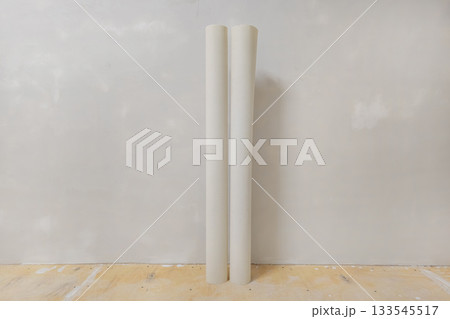 Two rolls of wallpaper stand against a gray wall Two rolls of wallpaper stand against a gray wall 133545517