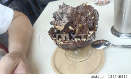 Chocolate ice cream sundae with brownie pieces and almond flakes in glass bowl, indulgent dessert moment 133546511