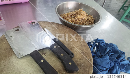 Kitchen cutting board with cleaver and knife, chopped shallot mix bowl, stainless counter, blue cloth, rustic food prep scene Kitchen cutting board with cleaver and knife, chopped shallot mix bowl, stainless counter, blue cloth, rustic food prep scene 133546514