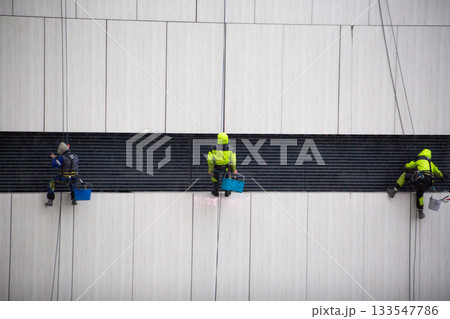 Team of industrial climbers works on wall of building. Cleaning ventilation and exhaust ducts with help of professional climbers. This is difficult and dangerous job with risk to life Team of industrial climbers works on wall of building. Cleaning ventilation and exhaust ducts with help of professional climbers. This is difficult and dangerous job with risk to life 133547786