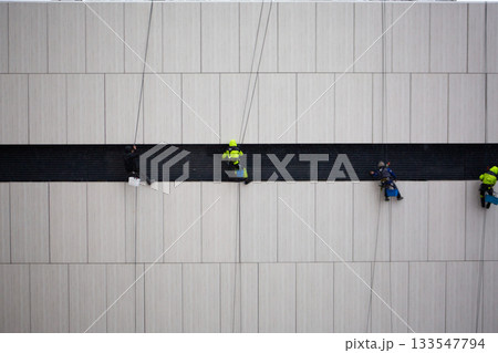 Industrial climbers at work. Cleaning building facade after construction. Dangerous profession at height during adverse weather conditions. Professional climbers in risky job 133547794