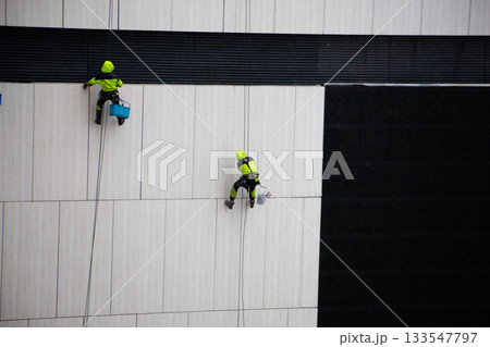 Climber in protective gear descends the side of building using special ropes, seat and safety equipment. This dangerous work is for real men. Phobia of heights 133547797
