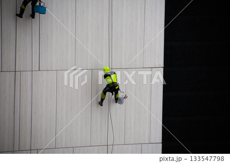 Climber in reflective protective suit uses ropes and safety equipment to descend the building facade during work. Concept of working at height and in challenging weather conditions 133547798