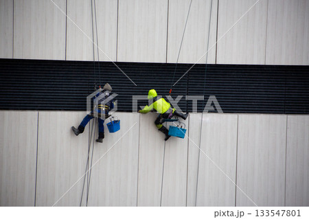 Climbers cling to safety ropes while performing dangerous work at construction site. Men wearing protective equipment in bad weather. Dangerous profession for men 133547801