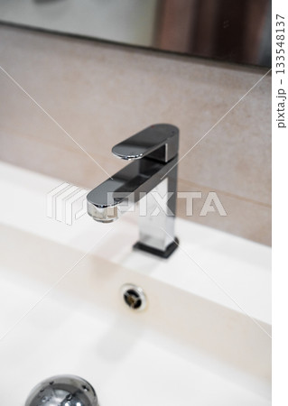 Close-up view of modern chrome bathroom faucet showcasing reflective metal surface and minimalist style Close-up view of modern chrome bathroom faucet showcasing reflective metal surface and minimalist style 133548137