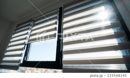 Zebra blinds illuminated by strong sunlight on high-rise apartment window with striped daylight pattern Zebra blinds illuminated by strong sunlight on high-rise apartment window with striped daylight pattern 133548145