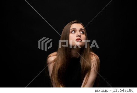 Studio portrait of young woman looking upward with thoughtful expression on black background Studio portrait of young woman looking upward with thoughtful expression on black background 133548196