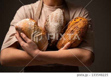 Baker holding three artisan bread loaves, showcasing variety, texture, and handcrafted quality 133548225