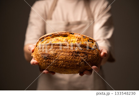 Baker holding seeded artisan loaf with raisins and golden crust Baker holding seeded artisan loaf with raisins and golden crust 133548230