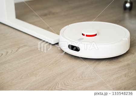 Robot vacuum cleaner moving under table while cleaning wooden floor with precise smart navigation system 133548236