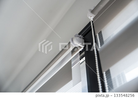 Detail of mounted zebra roller blinds with chain mechanism and striped fabric layers on interior window 133548256