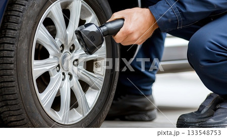 A mechanic is using a digital tool to check the tire pressure of a vehicle in a service area while it is daylight 133548753