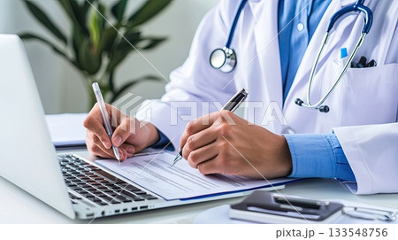A healthcare worker examines documents and writes notes while using a laptop in a professional office setting 133548756