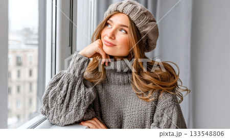 Woman poses thoughtfully by a window in a cozy sweater and beret during a rainy day in the city Woman poses thoughtfully by a window in a cozy sweater and beret during a rainy day in the city 133548806