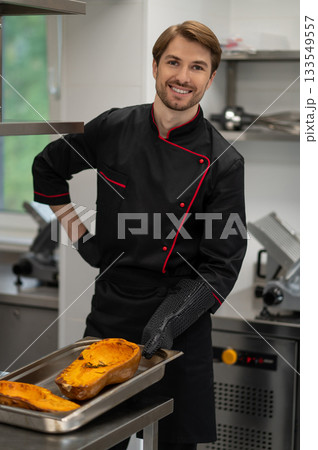 Cook holding tray with pumpkin in oven mitts in professional kitchen Cook holding tray with pumpkin in oven mitts in professional kitchen 133549557