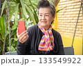 An elderly woman is sitting in a rocking chair in a park 133549922