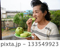 An old woman is eating guavas. 133549923