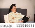 An old woman is reading a book on the bed 133549931