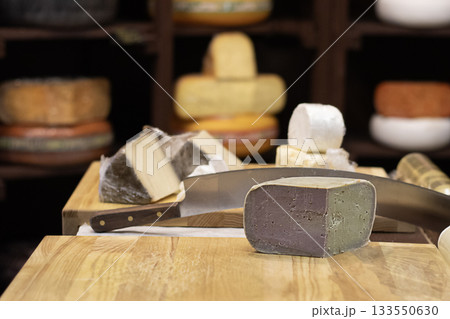 Assorted cheese blocks and knife on wooden board in a rustic cheese shop display Assorted cheese blocks and knife on wooden board in a rustic cheese shop display 133550630